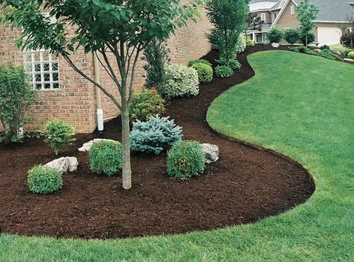 Curved dark mulch bed with shrubs and boulders along a brick home