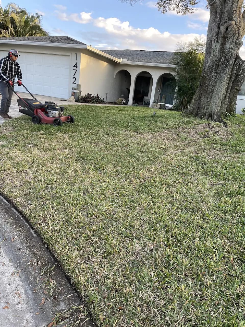 Crew member push mowing a lawn beside a stucco home